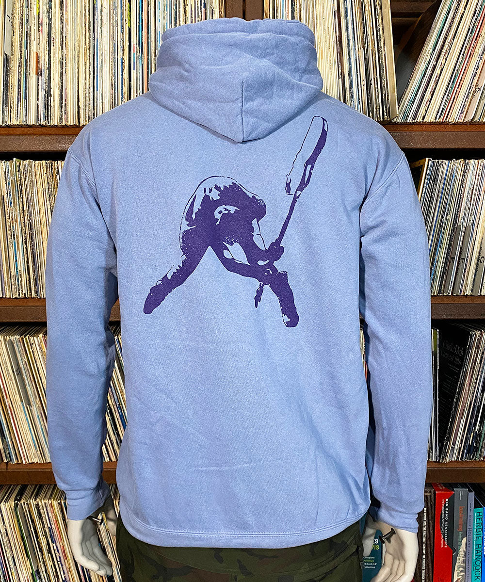 Light blue hoodie with a purple graphic on the back, worn by a person in front of a bookshelf.